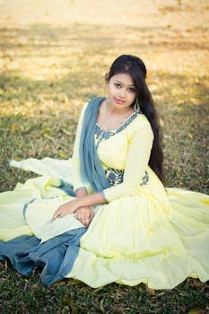 Portrait of a woman in traditional attire, sitting gracefully in a sunny park setting.